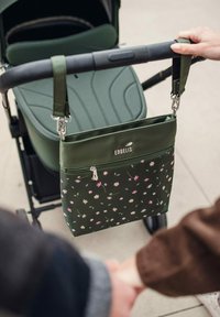 Zelená taška s květinovým potiskem a zipovou kapsou, připevněná k rukojeti kočárku, vyrobená z odolného materiálu, s pevnými sponami a logem značky.