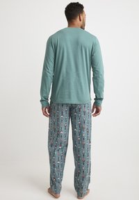 Blusa de manga larga en tono azul verdoso combinada con pantalones de pijama estampados que presentan diseños de cascanueces sobre un fondo azul. Material de algodón, ajuste relajado.