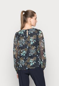 Blusa floral em tecido escuro e transparente, com flores em azul claro e verde, mangas longas e detalhe em forma de olho na parte de trás.