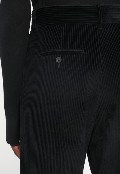 Black corduroy trousers with vertical ridges, featuring a side pocket and a two-button closure. The waistband has a textured design.