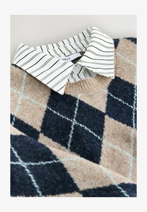Stickad tröja med ett mönster av tan och marinblå romber, med en vit randig skjorta under och ett texturerat, mjukt material.