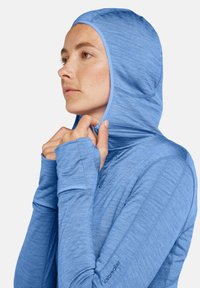 Sudadera de manga larga con capucha de color azul claro, hecha de un material texturizado, que presenta agujeros para los pulgares en las mangas y un diseño ajustado alrededor de la cara.