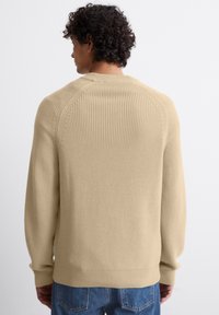Beige gestrickter Pullover mit geripptem Muster, Rundhals und leicht fallenden Schultern. Mit gerippten Bündchen und Saum abgeschlossen.