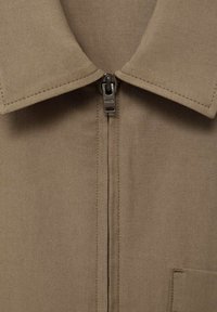 Giacca marrone con colletto, zip frontale e dettagli sulle tasche. Realizzata in tessuto resistente con cuciture in evidenza e una texture liscia.