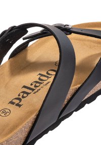 Sort lædersandal med krydsende remme, kork sål og gummisål. Har "palado" branding synlig på sålen.