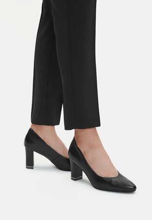 Czarne skórzane buty na wysokim obcasie z zaokrąglonym noskiem i masywnym obcasem, zestawione z dopasowanymi czarnymi spodniami. Gładka faktura, prosty design.