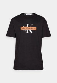 Sort bomulds T-shirt med en hvid "CK" logo og teksten "Calvin Klein Jeans" i et orange rektangel tværs over brystet. Korte ærmer, crewneck design.