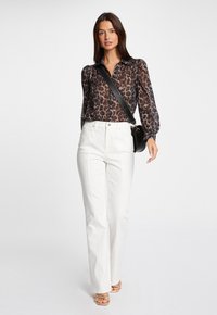 Chemise à manches longues, transparente, avec un motif léopard, associée à un pantalon taille haute blanc et des sandales dorées à lanières.