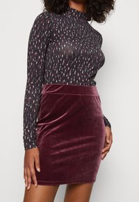 Top negro de manga larga con patrones rosa y blanco, combinado con una falda de terciopelo burdeos, con una textura suave y un diseño ajustado.