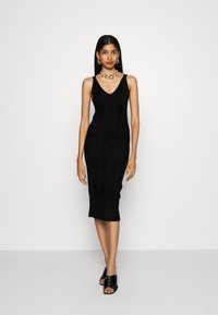 Black knitted bodycon dress featuring a V-neckline, textured pattern, and ribbed hem. Paired with black open-toe mules and chunky jewelry.