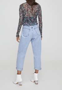Top lungo a maniche nere trasparenti con motivo floreale, abbinato a jeans a vita alta blu chiaro e stivaletti bianchi con tacco a blocco trasparente.