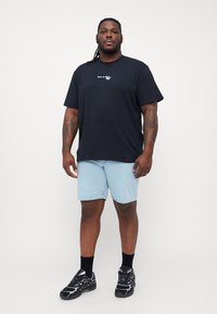 Svart kortermet t-skjorte med hvit tekst, kombinert med lyseblå denimshorts og svarte treningssko med lilla detaljer.