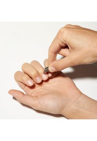 Mano destra che utilizza una piccola lama per pelare delicatamente uno strato sottile dall'unghia della mano sinistra.