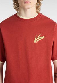 Camiseta de algodón roja con mangas cortas y un logo amarillo de Vans en el lado izquierdo del pecho, con un cuello acanalado color crema.