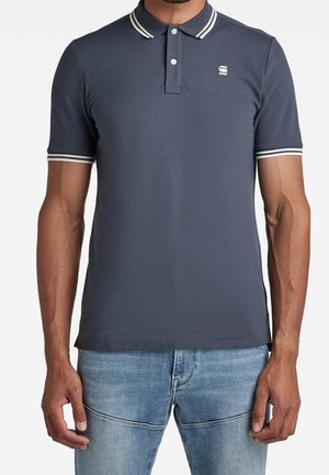 Granatowa koszulka polo wykonana z bawełny, z klasycznym kołnierzykiem, białymi kontrastującymi paskami na rękawach i małym logo na piersi.