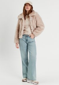 Veste en fausse fourrure rose clair, jeans bleus clairs à jambes larges et baskets beiges. Le pull présente une finition texturée avec de petites embellissements.