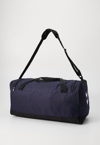 Mørkeblå og svart treningsbag med justerbar skulderrem og to sidelommer, vist mot en enkel hvit bakgrunn.