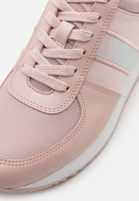 Baskets rose clair avec une tige en mesh texturé et cuir lisse, une semelle intermédiaire blanche contrastante, et une fermeture à lacets avec un accent réfléchissant.