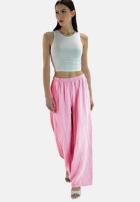 Rooie wijde broek van textuurstof met een trekkoord in de taille. Gepaard met een aansluitend wit tanktop en lichtgekleurde sandalen.