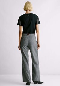 Camiseta negra con detalles de flecos en las mangas, combinada con pantalones anchos gris. Los pantalones presentan una tela texturizada y un detalle de bolsillo trasero.