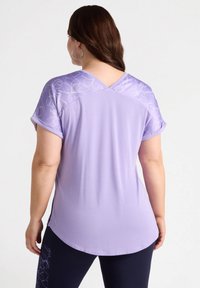 Lilla t-shirt med korte ærmer, blomstermotiv på den øverste ryg, rundet kant og sideslidser. Blødt materiale, afslappet pasform.