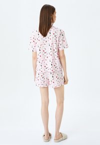 Pink pajamasæt bestående af en kortærmet top og shorts med et legesygt mønster af briller, saks og læber på en lys baggrund.