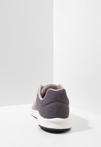 Scarpa sportiva con una tomaia in mesh grigio testurizzato, accenti rosa, colletto imbottito e una suola intermedia bianca; progettata per comfort e prestazioni.