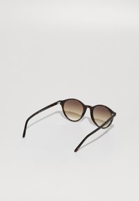 Ochelari de soare rotunzi cu ramă din plastic tartar și lentile degradate de culoare maro. Brațele subțiri de culoare neagră au accente lucioase, fiind realizate dintr-un material plastic ușor.
