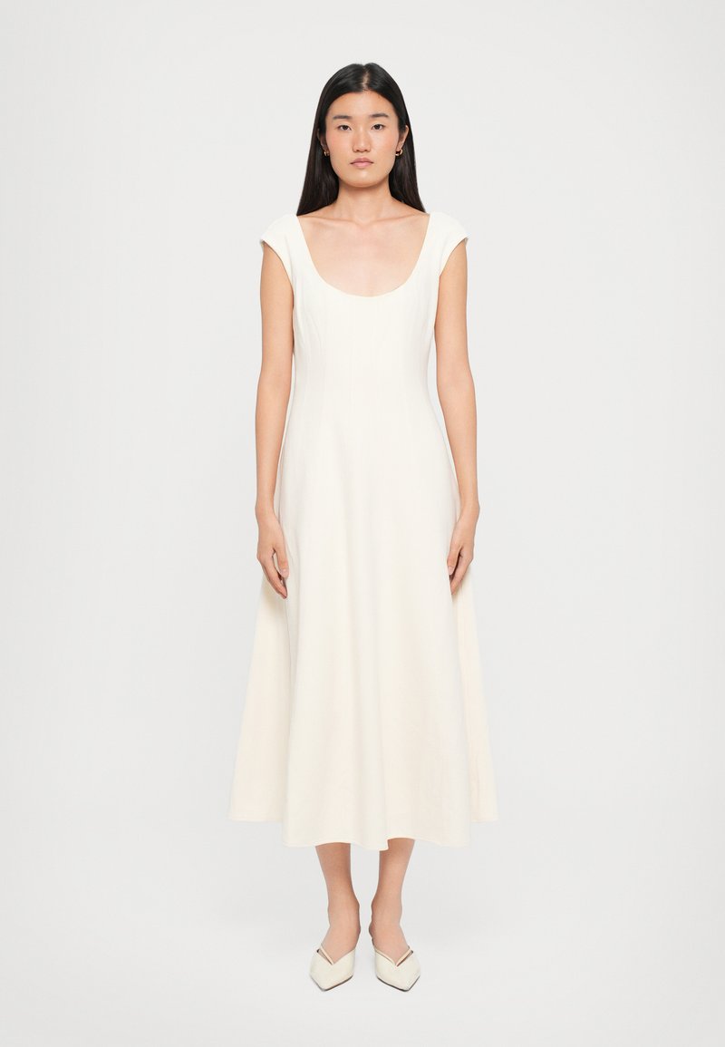 White scoop-neck dress made of smooth fabric, featuring cap sleeves and a flowing, mid-length skirt. Paired with pointed white shoes.