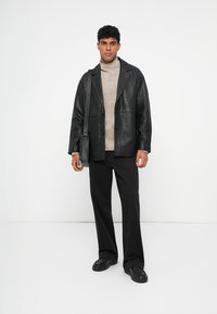 Giacca in pelle nera con colletto a punte, dolcevita beige a treccia, pantaloni neri a gamba larga e sneakers nere. Borsa a tracolla sulla spalla.