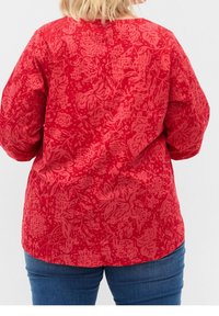 Camicia rossa con motivo floreale, con scollatura tonda e maniche lunghe, abbinata a jeans in denim blu.