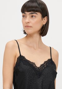 Sort satin camisole med blonder i halsen, der har et diskret leopardmønster. Stropperne er justerbare og slanke.