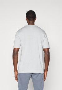 Ανοιχτό γκρι μπλουζάκι με κοντό μανίκι, στρογγυλή λαιμόκοψη και λεία υφή, φορεμένο με γκρι αθλητικά παντελόνια.