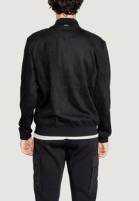 Giubbotto bomber in suede nero con colletto e polsini a coste, caratterizzato da una texture liscia e da dettagli di cucitura discreti sulla parte posteriore.