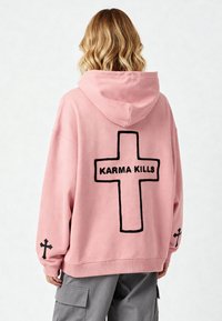 Felpa over-size rosa con ricamo nero a forma di croce e la scritta "KARMA KILLS" sul retro. Realizzata in tessuto morbido con polsini e orlo a coste.