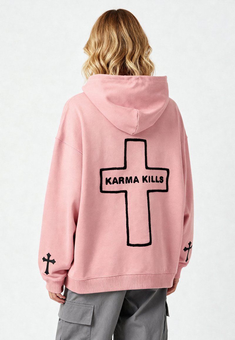 Felpa over-size rosa con ricamo nero a forma di croce e la scritta "KARMA KILLS" sul retro. Realizzata in tessuto morbido con polsini e orlo a coste.