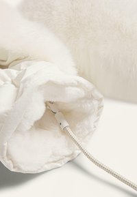 Pătură albă încălzită cu interior moale din blană artificială, cablu de alimentare asemănător cu o frânghie și un sistem de închidere alb. Textură exterioară netedă.