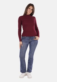 Maglione lungo a coste bordeaux a maniche lunghe abbinato a jeans blu aderenti e sneakers bianche, con un collo alto e una vestibilità slim.