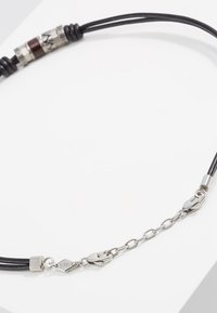 Schwarzes Lederhalsband mit metalischen Akzenten, das zylindrische Details und einen silbernen Verschluss beinhaltet. Enthält eine Kettenverlängerung zur Anpassung.