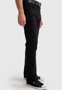 Vaqueros de mezclilla negros con corte slim, que cuentan con cinco bolsillos y una textura suave. Combinados con zapatillas de tela negras con acentos blancos.