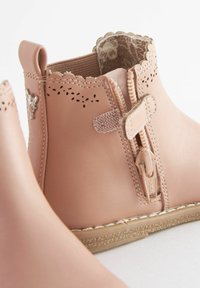 Botas de tobillo de cuero rosa con bordes en forma de ondas, cierre de cremallera lateral y una suela texturizada. El interior tiene un forro de patrón floral.