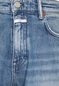 Světle modré džíny z denimu s klasickým designem pěti kapes, obsahující kovový knoflík, kontrastní šití a jemné detaily džínového omytí.