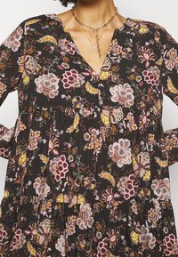 Blumenmusterkleid aus schwarzem Stoff mit lebhaften pinken, gelben und grünen Blumen. V-Ausschnitt-Design mit gerafftem Oberteil und fließenden Ärmeln.