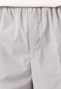 Grau gefärbte Hose aus leichtem Stoff, mit einem elastischen Bund, glatter Textur und einfachem Nahtdetail an der Seite.