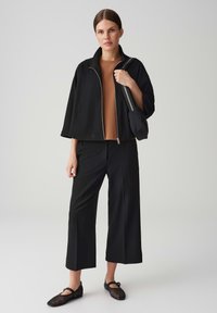 Black cropped jacket with silver zipper, brown top, wide-leg black pants, and black mesh flats. Accessories include a small black bag.