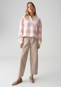 Gestreepte trui in roze en wit, met een kraag en laten schouders; gecombineerd met licht beige broek met wijde pijpen en zachte taupekleurige platte schoenen.