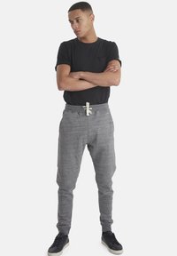 Camiseta negra con bolsillo, combinada con pantalones joggers grises con cierre de cordón. Llevada con zapatillas deportivas negras.