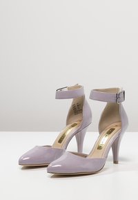 Escarpins en cuir synthétique lilas avec un bout pointu, une bride à la cheville, et un talon aiguille de 10 cm. Texture lisse avec une finition brillante.