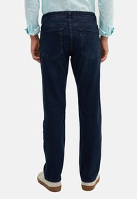 Dark blue denim jeans with a straight-leg design, dual back pockets, and a mid-rise waist. Styled with a light-colored shirt and shoes.