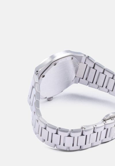 Ceas din oțel inoxidabil argintiu cu un brățară segmentată. Carcasa este octogonală, cu o finisare netedă și are șuruburi vizibile pe spate.